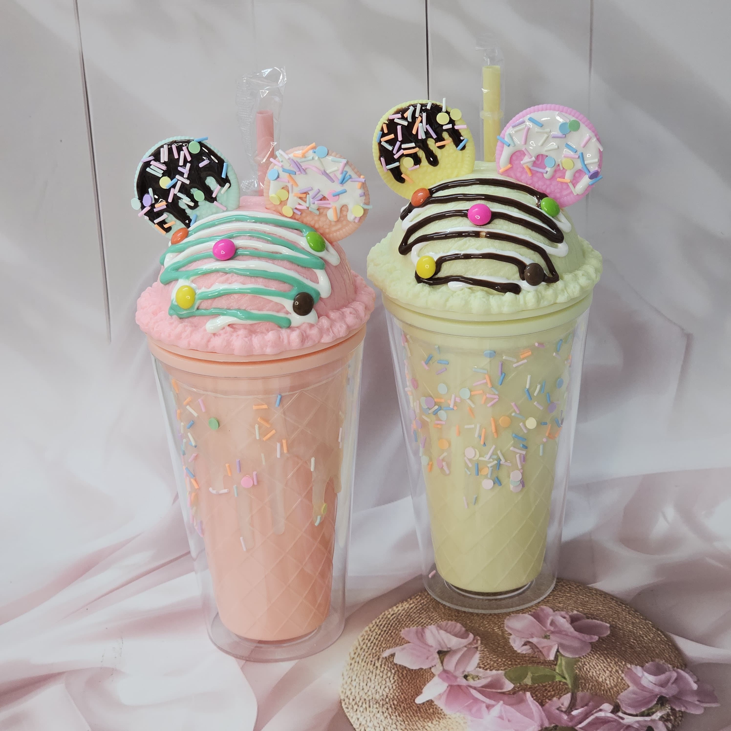 Two adorable Usmile Toys novelty tumblers, one pink and one lime green, each topped with a playful 'ice cream' lid decorated with colorful sprinkles and chocolate drizzle, complete with a straw and an Oreo-shaped charm. Perfect for kids' drinks and adding fun to everyday hydration." www.usmile.toys